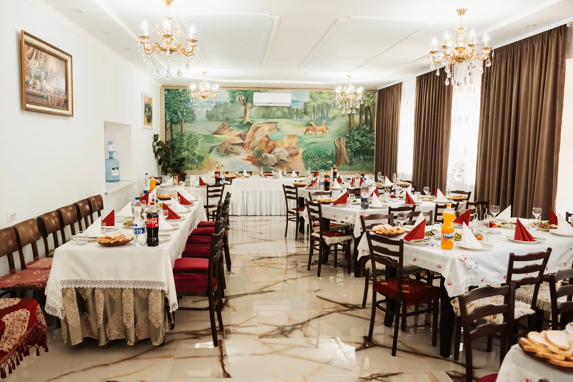 Restaurantul aranjat pentru un eveniment, cu mese lungi îmbrăcate în alb, șervete roșii, aperitive pregătite și candelabre de cristal
