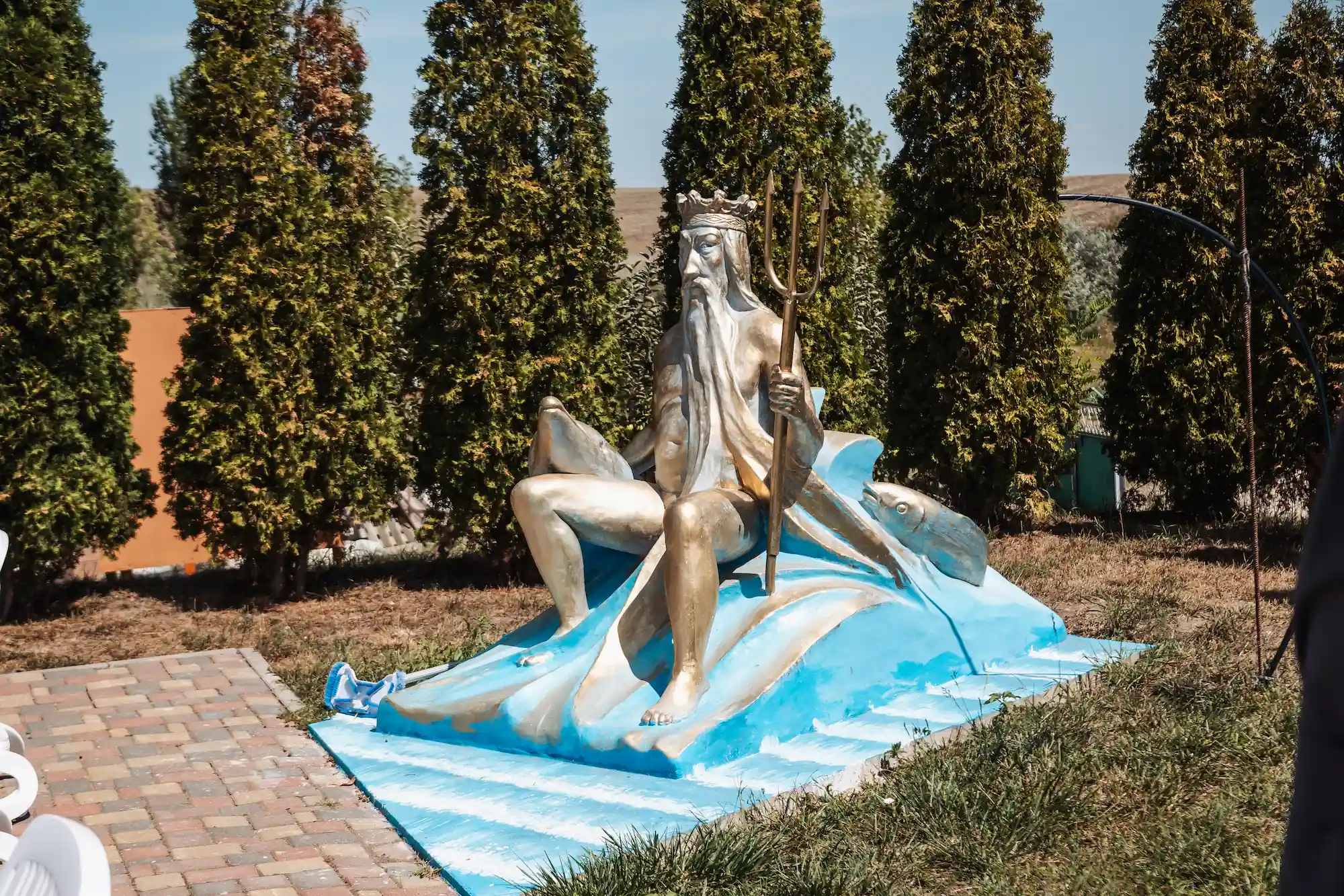 Statuie decorativă a lui Neptun, pe o cascadă de valuri, printre tuia din curtea pensiunii